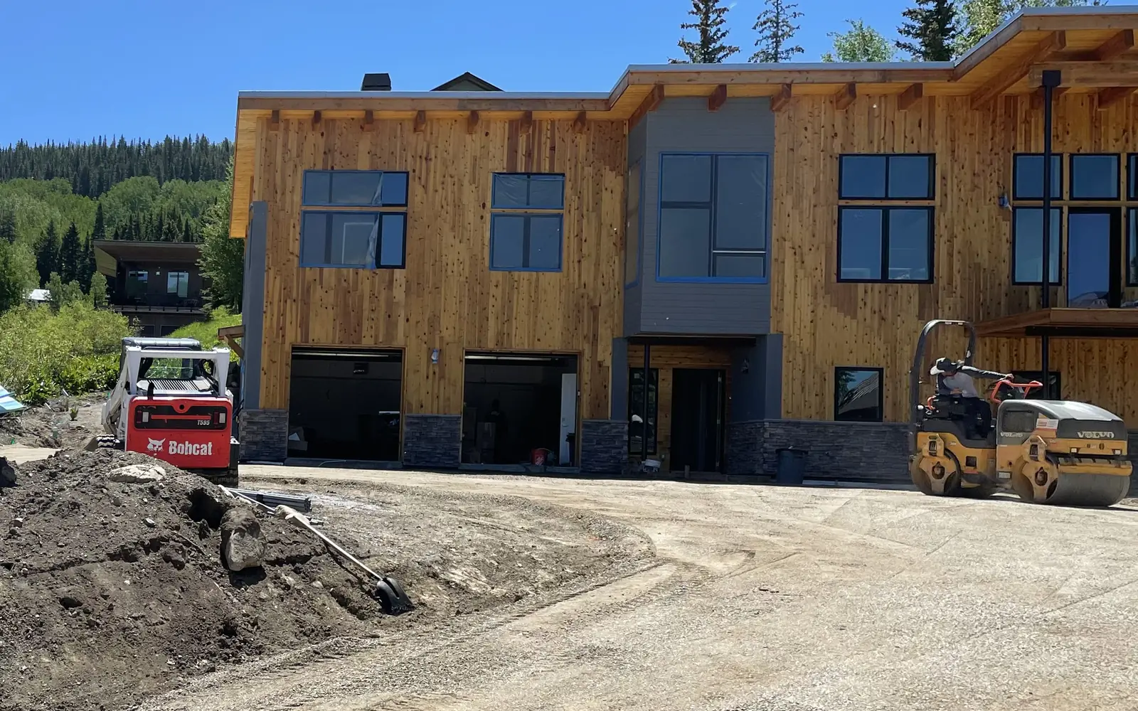 Before: bare dirt and gravel in front of a new timber-sided mountain home, with a skid steer and roller parked