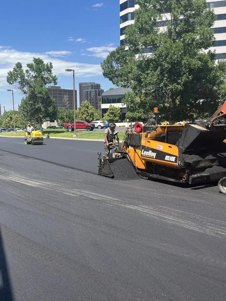 Paving machine laying a fresh asphalt mat across an office parking lot